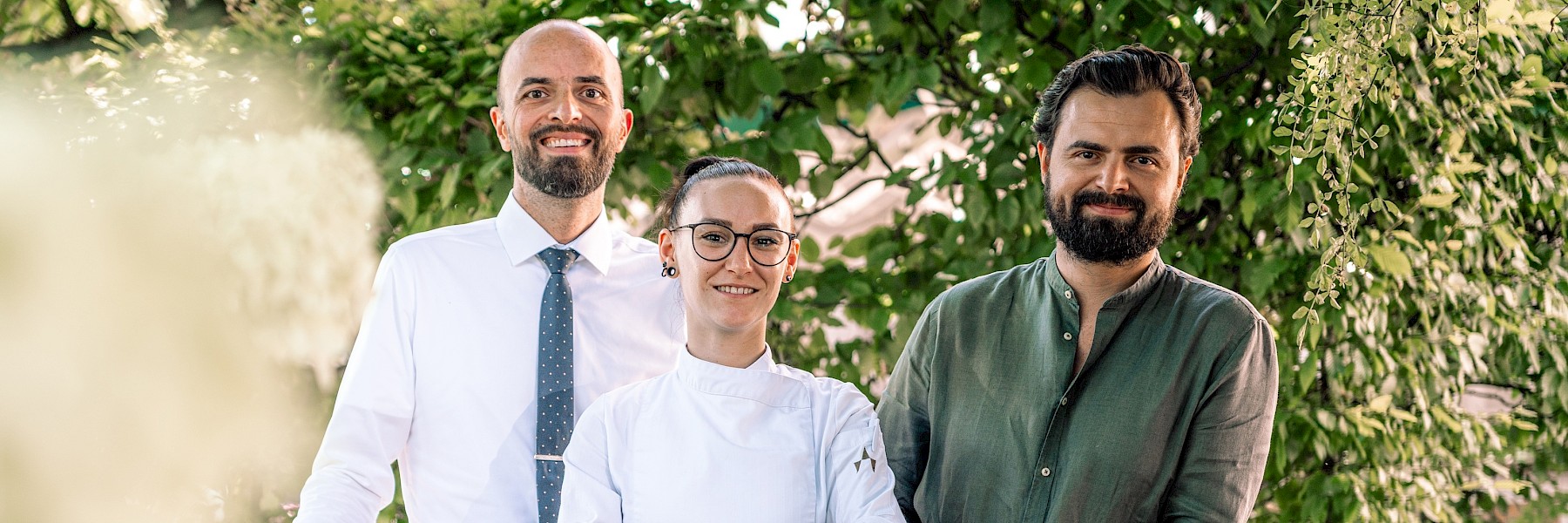 Dieses freundliche Empfangsbüro strahlt eine warme und einladende Atmosphäre aus. Zwei Mitarbeiterinnen sitzen lächelnd an modernen Computern hinter einem stilvollen Holztresen. Die Einrichtung kombiniert klassische Elemente wie goldgerahmte Spiegel, traditionelle Vorhänge und Jagdtrophäen mit moderner Technik. Tageslicht fällt durch ein großes Fenster, wodurch der Raum hell und freundlich wirkt. Eine grüne Pflanze bringt zusätzlich Leben in das Interieur. Die Szene vermittelt Professionalität, Herzlichkeit und Gastfreundschaft – der perfekte erste Eindruck für Gäste oder Kunden.