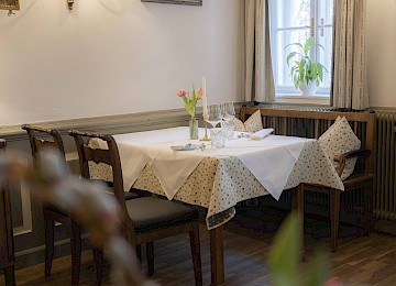 Das Bild zeigt einen elegant gedeckten Tisch in einem Restaurant oder Festsaal. Im Vordergrund steht ein Schild mit der Aufschrift „Reserviert“ in goldener Schrift auf dunklem Holz – ein Hinweis auf eine besondere Veranstaltung oder reservierte Gäste. Der Tisch ist mit weißem Tischtuch, kunstvoll gefalteter Stoffserviette, edlen Kristallgläsern und einer Vase mit frischen Tulpen dekoriert. Die warme Beleuchtung und die unscharf gehaltenen Elemente im Hintergrund schaffen eine gemütliche und einladende Atmosphäre. Dieses Arrangement vermittelt stilvolle Gastlichkeit und einen Hauch von Exklusivität – ideal für festliche Anlässe.