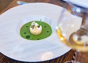 Dieses Gericht zeigt eine klassisch interpretierte Tafelspitz-Speise, stilvoll in einem Kupfertopf serviert. Zart gekochtes Rindfleisch liegt in einer klaren Brühe, begleitet von buntem Wurzelgemüse und frischen Kräutern. Um den Topf sind traditionelle Beilagen angerichtet: knusprige Röstkartoffeln, cremiger Spinat, Apfelkren und Schnittlauchsauce – alles liebevoll angerichtet in kleinen Töpfen und Schälchen. Die rustikale Holzunterlage betont den bodenständigen Charakter dieses österreichischen Klassikers. Die harmonische Zusammenstellung von Aromen, Texturen und Farben macht dieses Gericht zu einem herzhaften, authentischen Genusserlebnis.