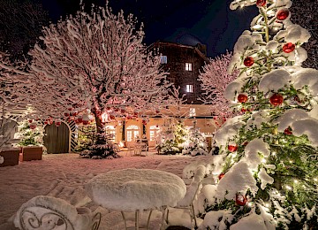 This winter scene captures a magical outdoor Christmas decoration. Numerous red ornaments hang from the snow-covered branches of large trees, creating vivid splashes of color against the white, snowy landscape. The shiny baubles reflect their surroundings and add a festive sparkle. The striking contrast between the deep red and soft white evokes a warm, holiday spirit. In the background, more trees and a snow-covered field enhance the peaceful, wintry atmosphere. This image beautifully embodies the charm of the Christmas season, blending natural beauty with classic holiday decoration.